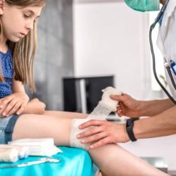 Medical female doctor bandaging young girl knee at the hospital